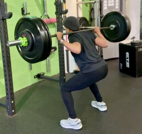 Jasmine Sandoval performing a barbell squat at the gym